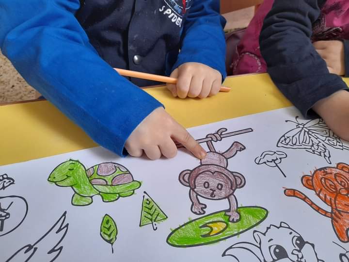 child wearing blue pointing at a brown monkey that has been colored on a page